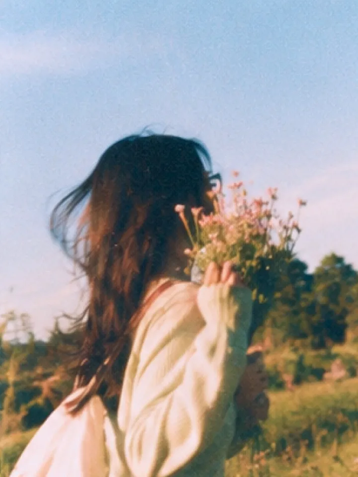 A woman holding a small bunch of wildflowers in a sunlit field